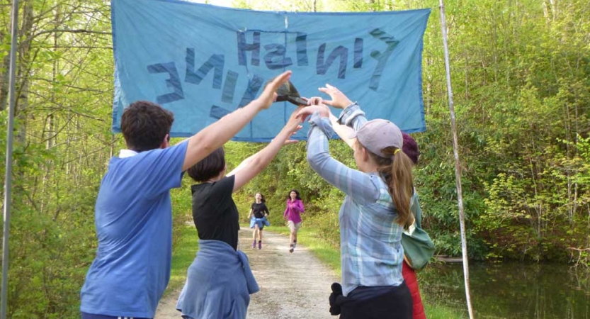 In the background, two students run forward toward a banner that appears to read "finish line." In font of the banner, four people make an archway with their lifted arms.